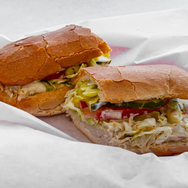 Two Jack's Pizza & Subs sandwiches, filled with meat, cheese, lettuce, tomatoes, and pickles.